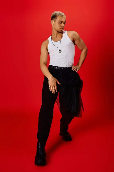 A young African American man poses stylishly in a red studio, showcasing a fashionable outfit. — Stock Photo