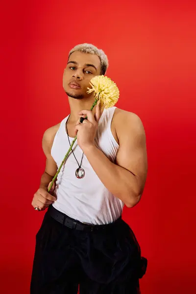 Un jeune homme élégant pose en toute confiance dans un studio rouge tout en tenant une fleur, exsudant charme. — Photo de stock