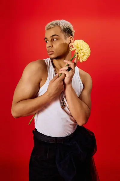 Young man with dyed hair poses confidently in a stylish tank top holding a flower. — Stock Photo