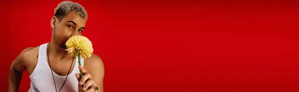 A young African American man poses playfully with a flower against a vibrant red background, banner — Stock Photo