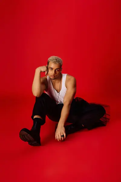A young man showcases trendy fashion in a striking red studio environment, exuding confidence. — Stock Photo