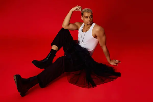 A young Black man poses confidently in a tank top and black pants against a red backdrop. — Stock Photo