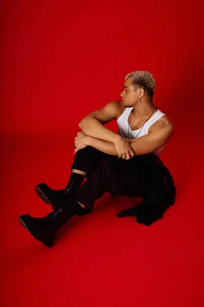 Un jeune homme aux cheveux teints pose avec confiance dans un studio rouge, mettant en valeur la mode à la mode. — Photo de stock
