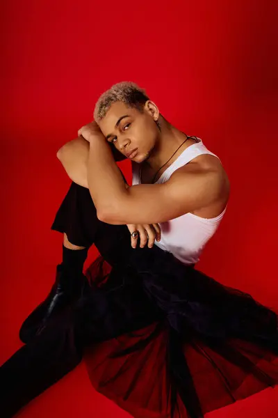 Un jeune homme noir élégant en débardeur et pantalon noir pose en toute confiance dans un studio rouge. — Photo de stock