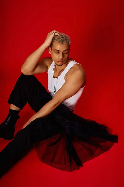 A young man with dyed hair showcases his fashion sense in a vibrant red studio. — Stock Photo