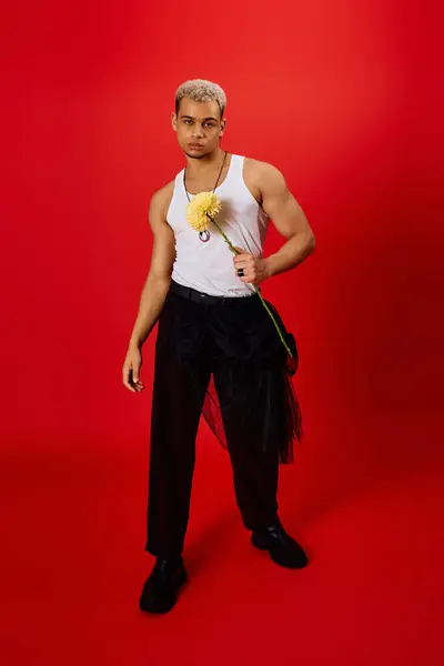 A young African American man confidently poses in a red studio, holding a flower. — Stock Photo