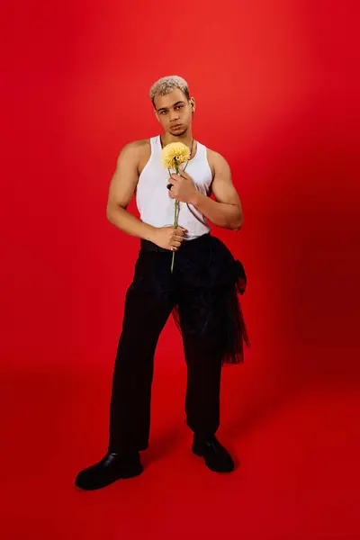 A young man with dyed hair stands confidently, holding a flower in a vibrant studio. — Stock Photo