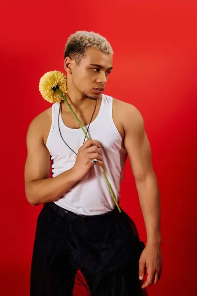 A young African American man poses confidently, showcasing his trendy fashion in a red studio. — Stock Photo