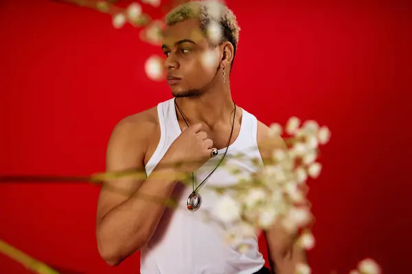 Un jeune homme à la mode aux cheveux teints pose en toute confiance dans un studio rouge, mettant en valeur son style. — Photo de stock