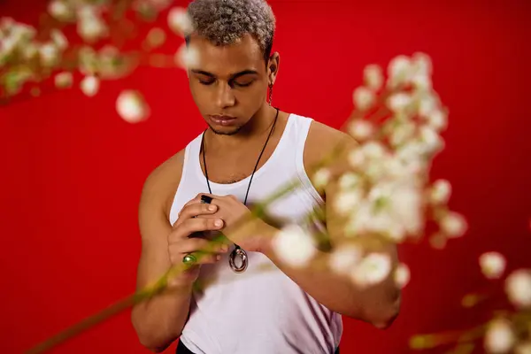 Un jeune homme aux cheveux teints pose avec confiance dans un débardeur, entouré d'une toile de fond rouge frappante. — Photo de stock