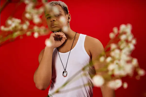 A young African American man confidently poses in a bright red studio in a tank top and black pants. — Stock Photo