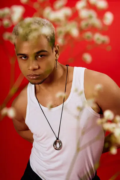 Ein stylischer junger Mann posiert selbstbewusst in einem roten Studio mit Tank-Top und schwarzer Hose. — Stockfoto