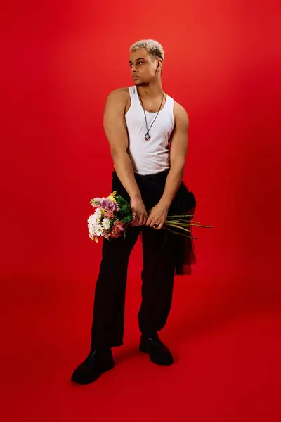 Young man showcases fashion and style, holding flowers in a vibrant red environment. — Stock Photo