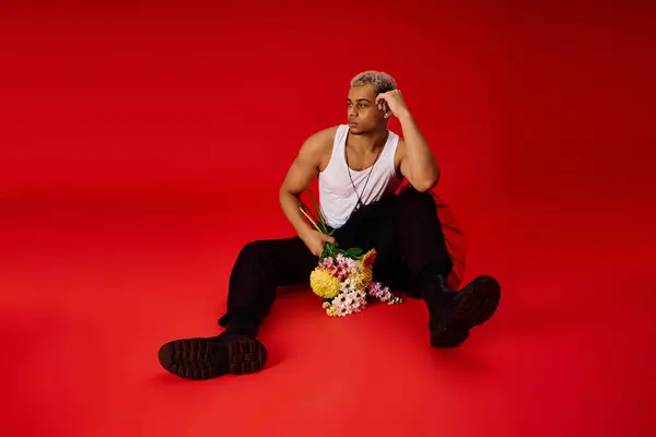 Un joven negro muestra su estilo en un estudio rojo brillante, sosteniendo flores. — Stock Photo
