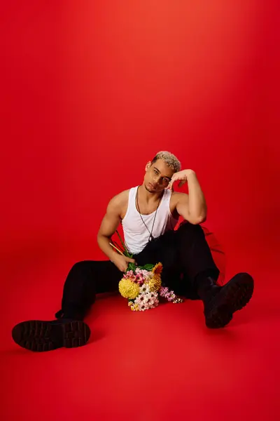 A young Black man with trendy dyed hair poses confidently in a red studio. — стоковое фото