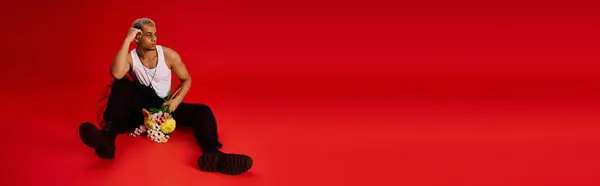 Un joven con estilo posa con confianza en un estudio rojo, mostrando su atuendo de moda y cabello, pancarta — Stock Photo