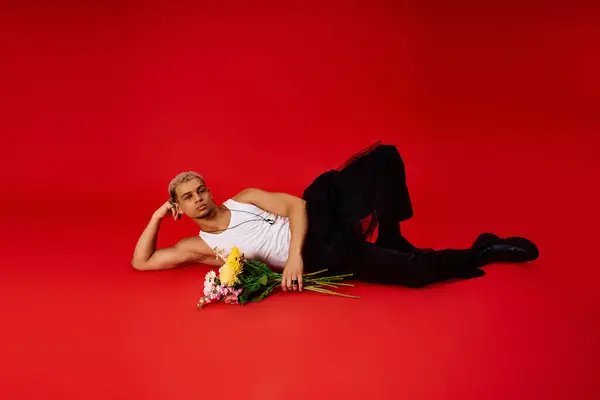 A young and handsome African American man lounges in a red studio, holding colorful flowers. — Stock Photo