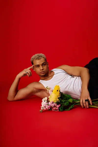 A fashionable young man relaxes on the floor, showcasing his style with flowers. — Stock Photo