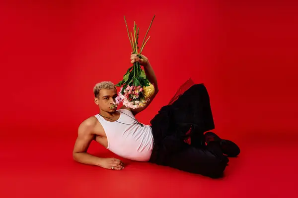 A young, stylish African American man in a tank top lounges in a vibrant red studio. — стокове фото