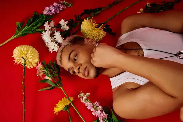 A young Black man with dyed hair poses in a tank top among flowers. — Stock Photo