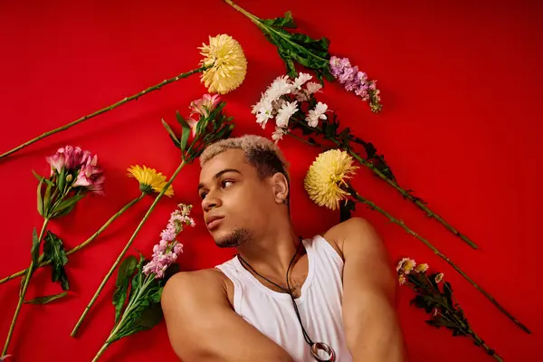 Ein selbstbewusster junger Mann präsentiert seinen Stil in einem Tank-Top, umgeben von bunten Blumen in einem Atelier. — Stockfoto