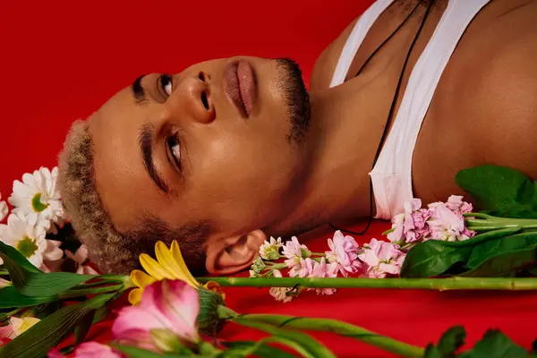 A young, handsome Black man poses confidently in a vibrant red studio decorated with flowers. — Stock Photo