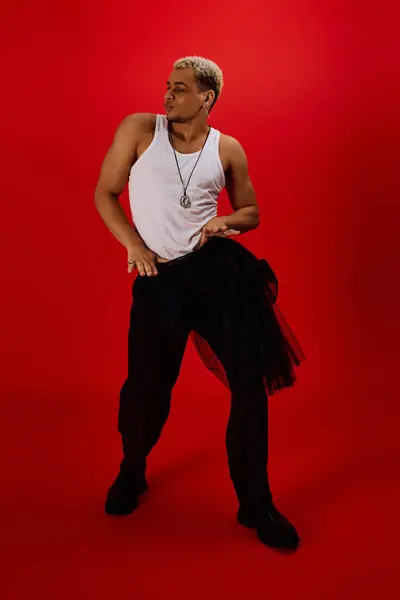 Un jeune homme élégant pose en toute confiance dans un studio rouge, mettant en valeur la mode à la mode avec les cheveux teints. — Photo de stock