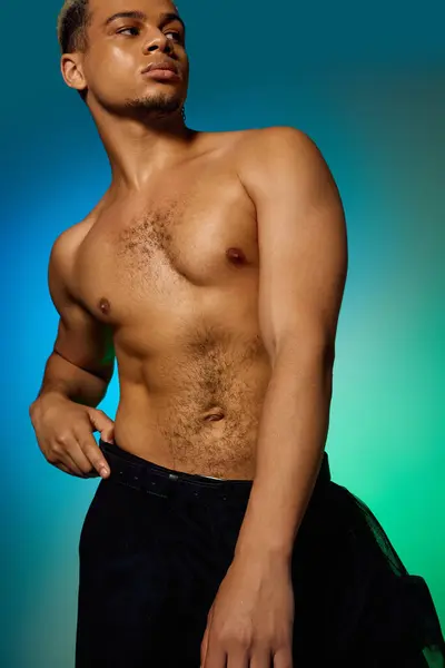 A confident young Black man poses shirtless in a colorful studio, showcasing his fashion. — Stock Photo