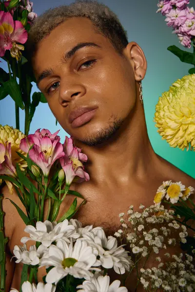 A young shirtless Black man with dyed hair poses among vibrant flowers in a studio. — Stock Photo