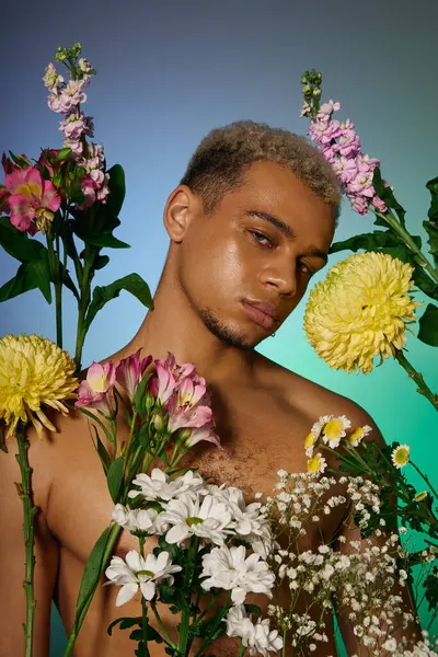 Ein junger Afroamerikaner ohne Hemd posiert selbstbewusst zwischen bunten Blumen und versprüht Charme. — Stockfoto