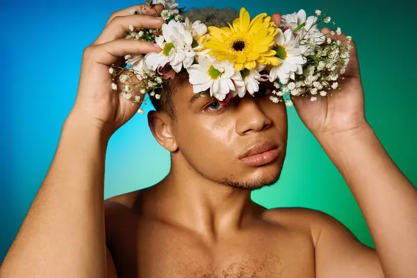 Un joven negro sin camisa lleva una corona floral en un colorido ambiente de estudio. - foto de stock