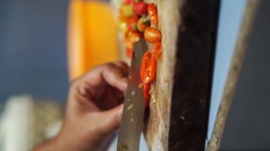 Kırmızı biberi mutfak bıçağıyla dilimleyen bir kadının dikey videosu.