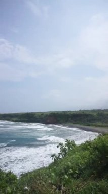 Gün boyunca büyük dalgalarla dolu mavi deniz suyuyla dolu bir sahilin güzel dikey videosu.