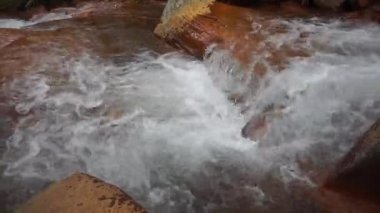 Dağlardan akan temiz nehir suyu ve turuncu kayalarla kaplı yeşil ağaçlar.