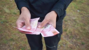 Bir kadının elleri bir çiftlikteki açık bir alanda yüz bin rupia sayıyor.