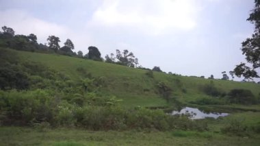 Doğal manzara dağları, doğal panorama tepeleri, ve uzun yeşil ağaçlardan oluşan ormanlar ve bulutlu mavi gökyüzünün altında yeşil tarlalar.
