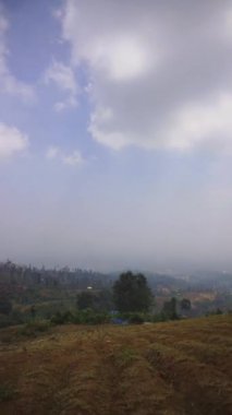 Doğal manzara dağları, doğal panorama tepeleri, ve uzun yeşil ağaçlardan oluşan ormanlar ve bulutlu mavi gökyüzünün altında yeşil tarlalar.