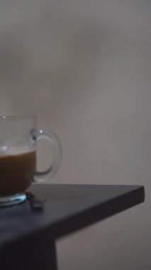 Beyaz bir bardakta, siyah bir masada bir fincan sütlü kahvenin dikey portresi.