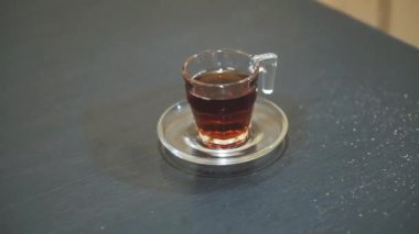 Siyah bir masanın üzerine beyaz cam bir fincana çay döküyorum.