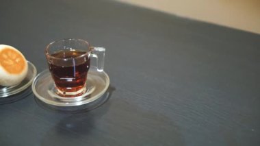 Bir fincan çay ve yeşil fasulye ekmeği, siyah masada yemeye hazır.