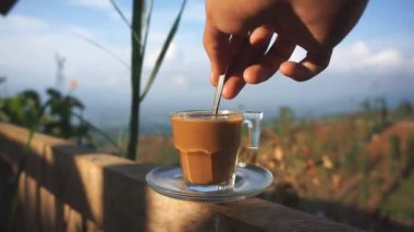 Dağlarda beyaz bardakta karıştırılmış bir fincan sütlü kahvenin güzel dikey görüntüsü.