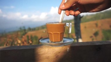 Dağlarda beyaz bardakta karıştırılmış bir fincan sütlü kahvenin güzel dikey görüntüsü.