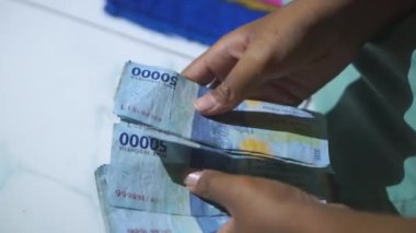 Bir çocuğun elleri geceleri evde elli bin rupia banknot sayıyor.