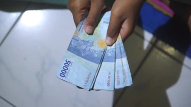 Bir çocuğun elleri geceleri evde elli bin rupia banknot sayıyor.