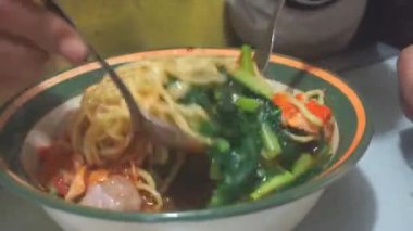 Bir adam kaşık ve çatal kullanarak tavuklu erişteli köfte yiyor.