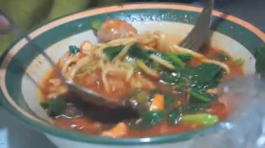 Bir adam kaşık ve çatal kullanarak tavuklu erişteli köfte yiyor.