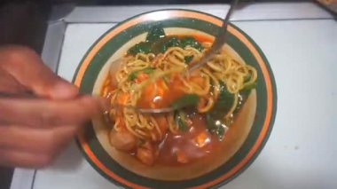 Bir adam kaşık ve çatal kullanarak tavuklu erişteli köfte yiyor.