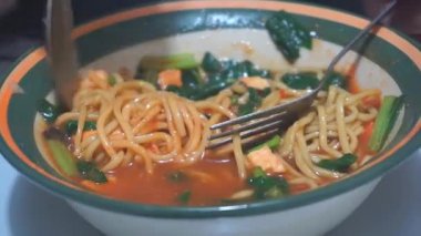 Bir adam kaşık ve çatal kullanarak tavuklu erişteli köfte yiyor.