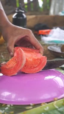 Bir adam kırmızı guava soyuyor ve kesiyor, ya da Latin Psidium guajava 'da, mutfak bıçağıyla..
