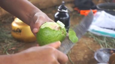 Bir adam kırmızı guava soyuyor ve kesiyor, ya da Latin Psidium guajava 'da, mutfak bıçağıyla..